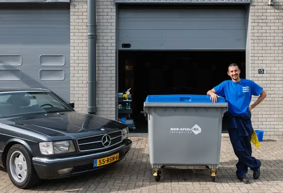 Ondernemer met 1100 liter rolcontainer bij autogarage